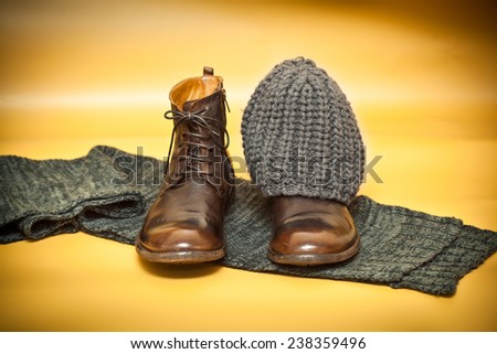 Brown fashion leather shoes, knitted scarf and cap on an abstract background yellow. still life of clothes