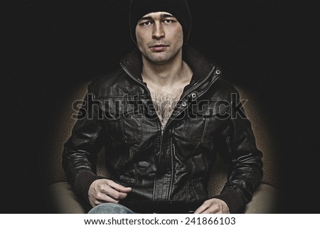 Brutal man in a hat and leather jacket on a black background
