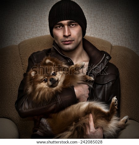 Brutal powerful man in a hat and leather jacket with a dog in her arms