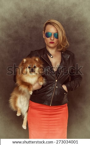Fashionable woman in a leather jacket, sunglasses and a red skirt keeps the dog in her arms. Photo stylized retro