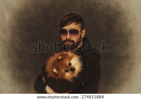 Brutal man with a beard and fashionable hairstyle with a dog in her arms. vintage style