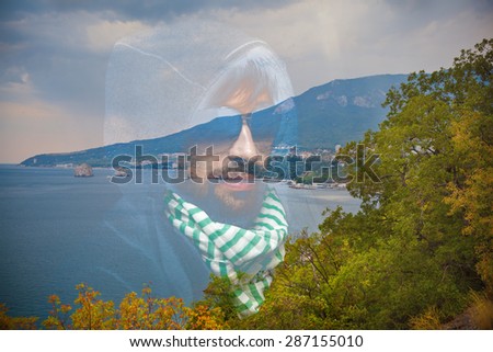 Portrait of a man in the hood, neck scarf and sunglasses. Summer landscape - sea, mountains and trees. Apply effect of double exposure.