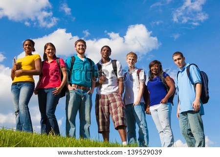 A group of diverse college students/friends outside on a hill with a sky background