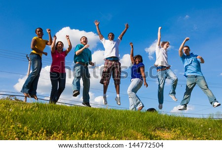 A group of diverse college students/friends jumping in the air outside on a hill