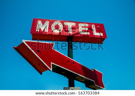 A vintage red neon hotel sign with a red arrow and a sky blue background