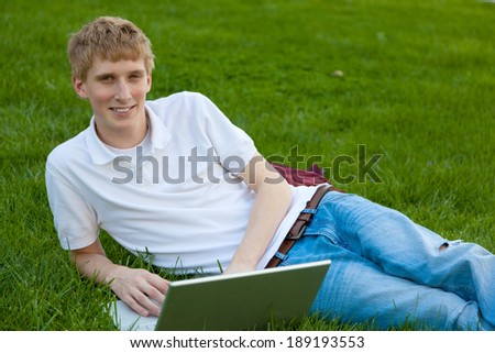 A young college age boy with a laptop computer sitting on grass outside