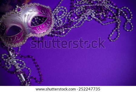 A purple mardi gras mask on a purple background with beads.  Carnivale costume.