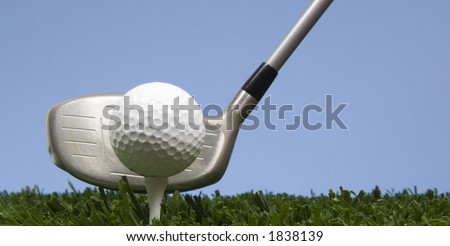 golf ball on tee on grass with blue sky with a driver