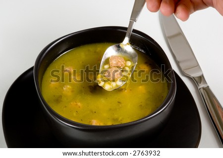 Bowl of Italian Wedding soup on white in black bowl with flatware