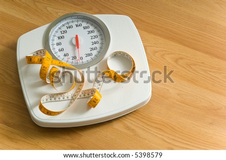 Bathroom scales with a large dial and a tape measure on a wooden floor with area to the left for copy