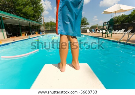 Young boy standing on the end of a diving board at a swimming pool