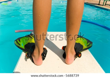 Child standing with flippers on the end of a diving board at a swimming pool