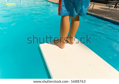 Young boy standing on the end of a diving board at a swimming pool - seems to be a little apprehension