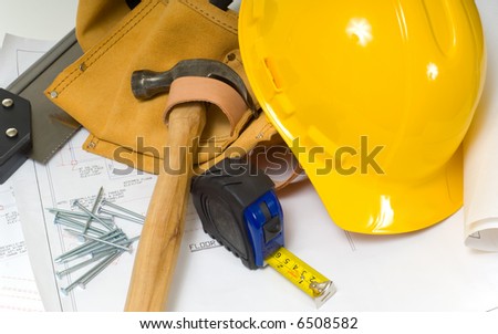 Items used by a construction worker including a leather tool belt, a hammer, a tape measure, tools, floor plans and a yellow hard hat