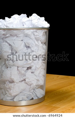 An overflowing waste basket full of crumpled pieced of paper