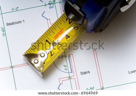 A tape measure slightly open lying on top of a house floor plan, construction industry or real estate