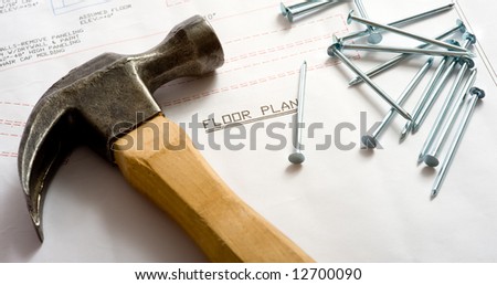 A hammer and nails lying on top of a house floor plan or blue print.  Construction industry or home construction business.