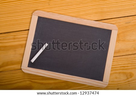 A blank school chalkboard or slate on a wood panel background with  a piece of white chalk, with copy space