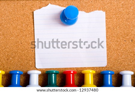 A torn white note stuck to a bulletin board with an over-sized push pin, with a row of push-pins or tacks below.  with copy space