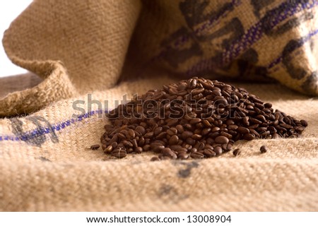 Roasted Coffee beans lying on top of a brown burlap coffee bean transportation bag, writing on bag says \
