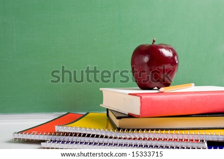 A stack of school books and an apple in front of a  blank chalkboard or blackboard background with copy space