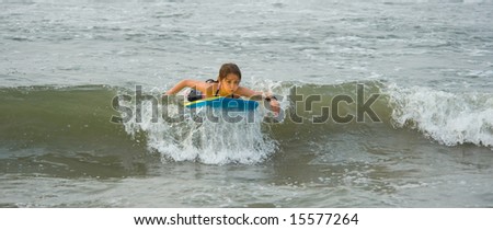 A young girl riding a boogie board in the ocean, having fun a displaying determination