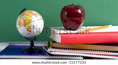 A stack of school books and an apple and a miniature globe in front of a  blank chalkboard or blackboard background with copy space