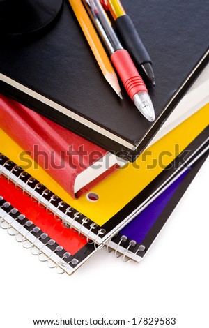 A stack of school books and spiral notebooks with a pencil and pens on tops in front of a white background