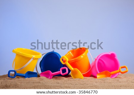 a row of colorful beach buckets or pails with shovels on a sandy beach with blue sky background with copy space