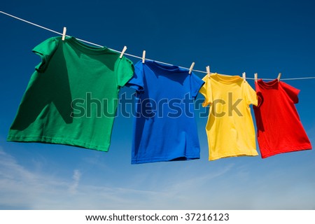 A group of primary colored t-shirts on a clothesline in front of blue sky