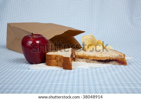 A students sack lunch with a peanut butter and jelly sandwich, potato chips and an apple