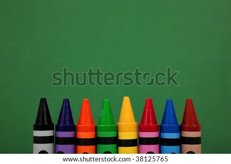 Assorted crayon tops with a green chalkboard background