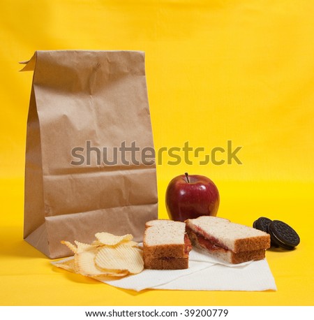 A sack lunch with peanut butter sandwich with apple, chips and cookies