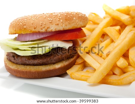 Hamburger with red onion, tomato and lettuce on a sesame seed bun with french fries on a white plate
