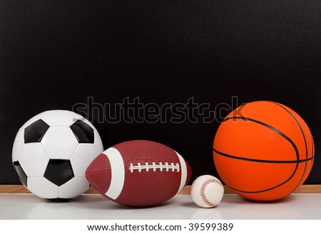 Assorted sports balls including a basketball, american football, soccer ball and baseball on a black chalkboard background