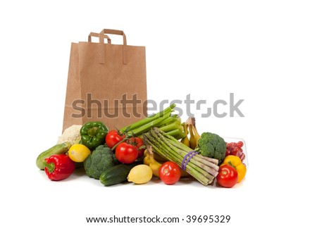 Assorted vegetables and fruits including asparagus, celery, tomatoes, peppers, bananas, lemons, cauliflower, cherry tomatoes, broccoli, cucumber and squash with a grocery sack on a white background