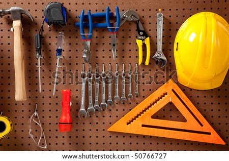 Peg board with hardhat, extension cord, flashlight, hammer, screw driver, caution tape, carpenter\'s square and pliers