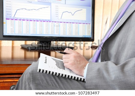 Businessman with Business plan.  Male hand with pen  on the  Business plan in front of computer screen with financial data and charts