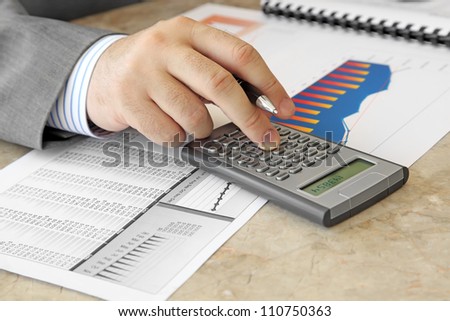 Businessman with Calculator Male Hand with Pen Using Calculator on the Table with Charts