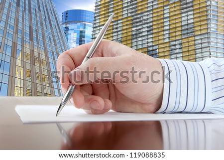Businessman's Hand with Pen on the Office Buildings Background