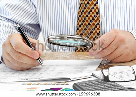Male Hands with Pen and Magnifying Glass  Analyzing  Financial Data  in the Office