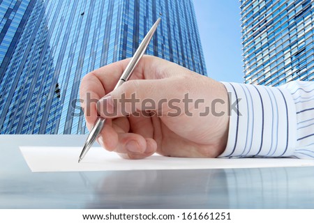 Businessman\'s Hand with Pen on the Office Buildings Background