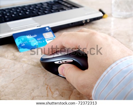 Credit card, laptop and computer mouse with male hand on the table .
