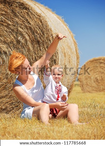 Young woman and little son on the field with big hay bale rolls