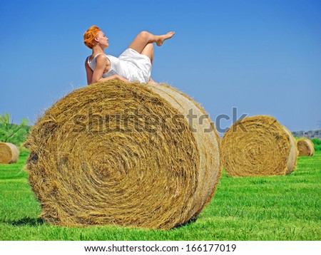 Young woman having fun on the field with big hay bale rolls