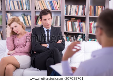 Unhappy couple talking to the psychologist and sitting on the couch