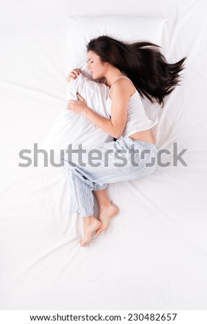Woman sleeping in fetal position with pillow