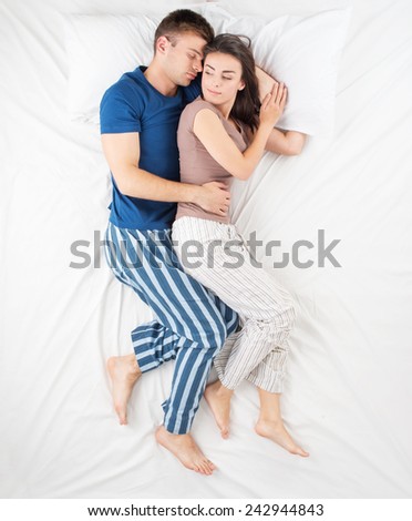 Top view photo of sleeping young couple in bed. Man hugging his smiling wife from the back