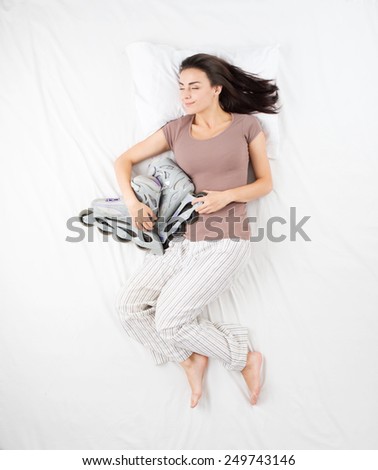 Smiling woman sleeping in a big white bed in an embrace with roller skates. Concept for dreams during sleep about sports and hobbies