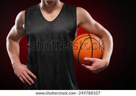Close up photo of a young male basketball player gripping the ball tightly with one hand on red background